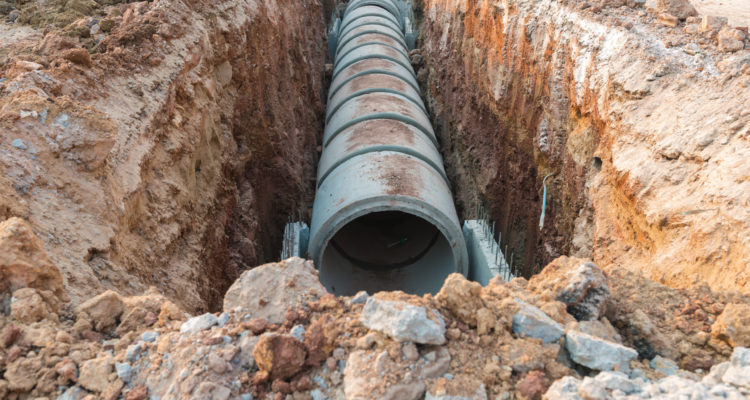 Row of concrete drainage pipe under earth near the construction site.